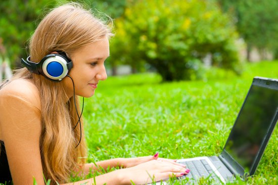 chica tumbada sobre el césped escuchando música con su ordenador
